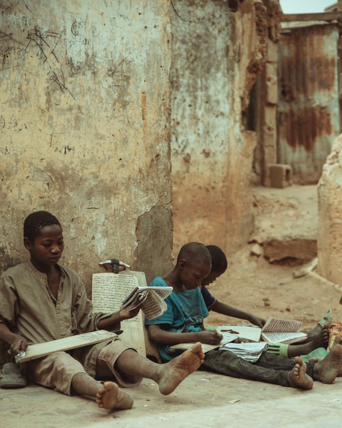 Services Children sit on city street engaged in reading and learning activities.
