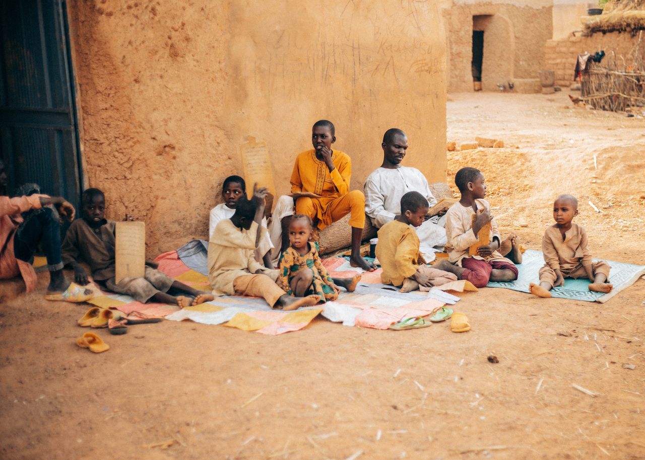 Services A group of African children and elders engaged in learning activities in a rural outdoor setting.