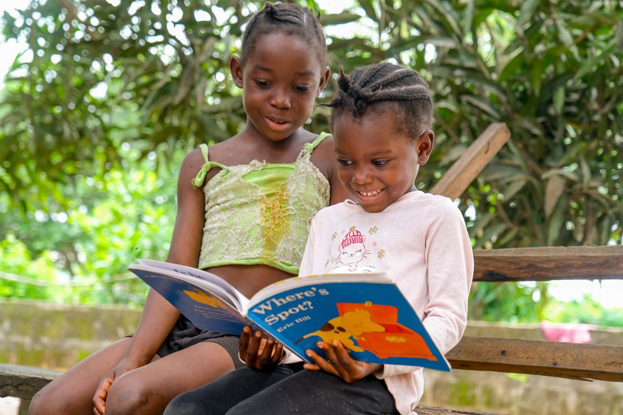 Services Two children enjoying a storybook outdoors, sharing a joyful reading moment.