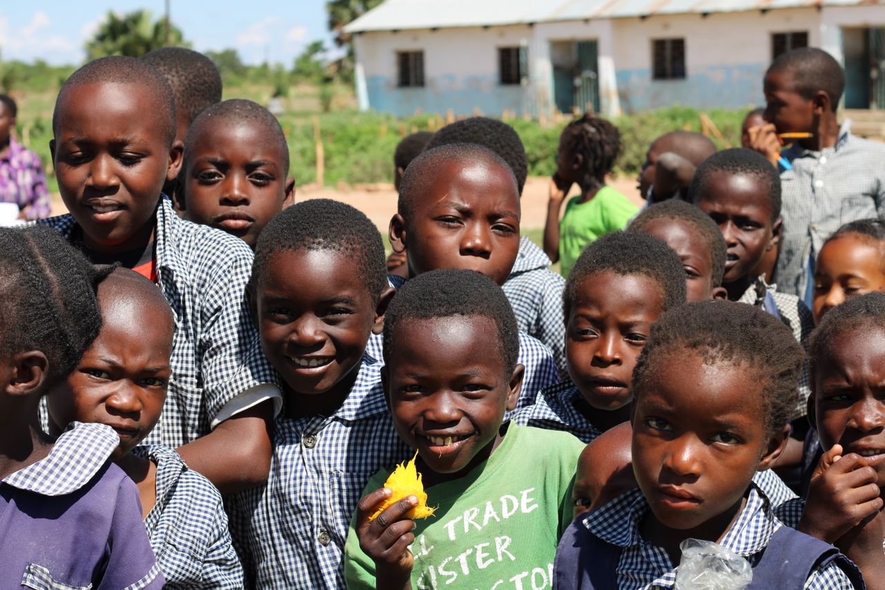 Services Happy group of children in a Zambian schoolyard on a sunny day.